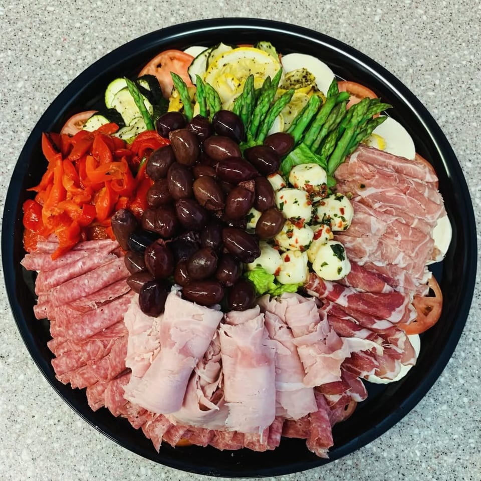 A large platter of antipasto with meats, cheeses, olives, roasted peppers, and grilled vegetables.