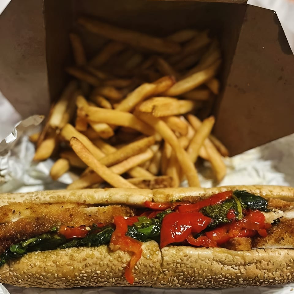 A Brynn Bradley cheesesteak with red peppers and greens, served with a side of golden fries.