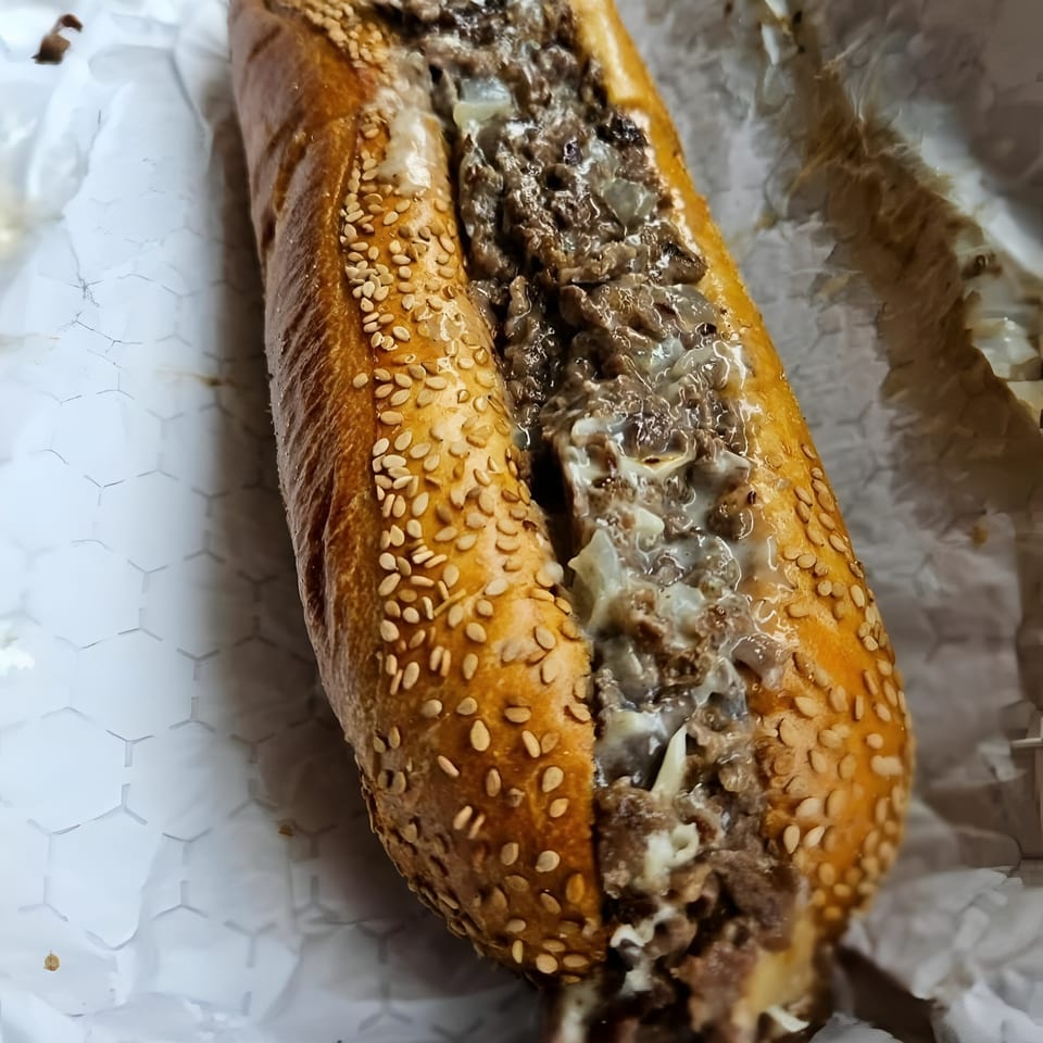A close-up of a Brynn Bradley cheesesteak, featuring steak, onions, and melted cheese on a sesame seed roll.