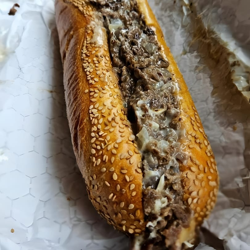A close-up of a Brynn Bradley cheesesteak, featuring steak, onions, and melted cheese on a sesame seed roll.