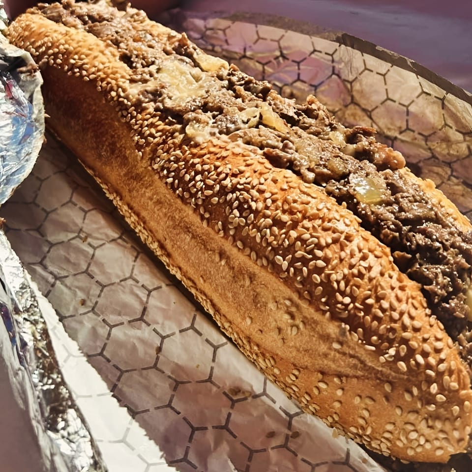 A Brynn Bradley cheesesteak, featuring a sesame seed bun filled with steak and cheese, wrapped in paper.